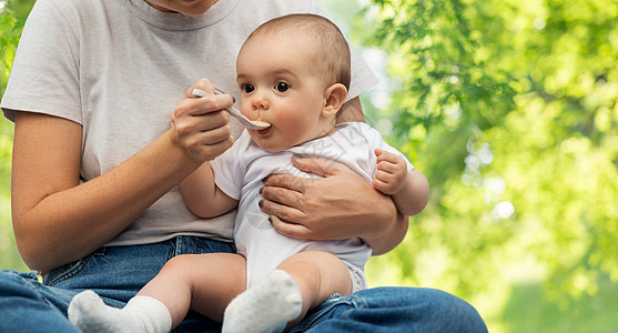 孩子,饮食食物的母亲用勺子喂养小婴儿绿色的自然背景用勺子喂小宝宝来亲近妈妈图片