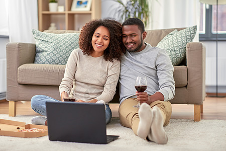休闲,人技术快乐的非裔美国人夫妇带着笔记本电脑外卖比萨饼,家喝红酒幸福的夫妇带着笔记本电脑家喝红酒图片