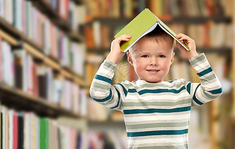 阅读,教育童年的微笑的小男孩的肖像,头上有书,屋顶上有图书馆背景微笑的男孩,带着书图书馆头上图片