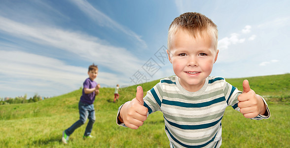 童年,手势夏天的微笑的小男孩穿着条纹衬衫,蓝天草地背景上竖起大拇指微笑的男孩户外竖起大拇指图片