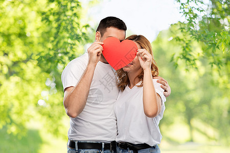 爱,情人节人际关系的微笑的夫妇躲红色的大心脏后面绿色的自然背景微笑的夫妇躲大红的心后面图片