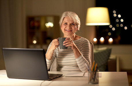 技术,老年人人的快乐的老年妇女带着笔记本电脑晚上家喝咖啡带着笔记本电脑家喝咖啡的高级女人图片