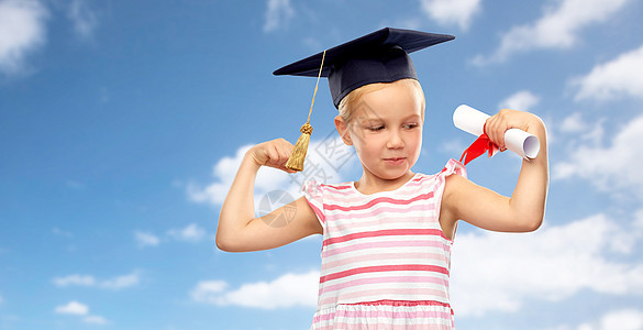 学校,教育学理念快乐的小女孩戴着学士帽或沙黑板,有蓝天云彩背景的文凭有文凭的灰泥板上的小女孩图片