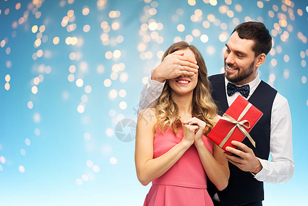 情人节,情侣,人际关系人的快乐的男人给女人惊喜的礼物,蓝色背景下的节日灯快乐的男人给女人惊喜的礼物图片