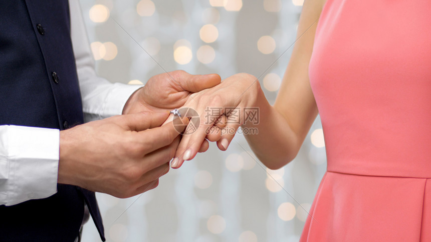 ‘~订婚,求婚人的近距离的男人把钻石戒指戴表妹的手指上的假日灯光背景男人把订婚戒指戴表妹的手指上  ~’ 的图片