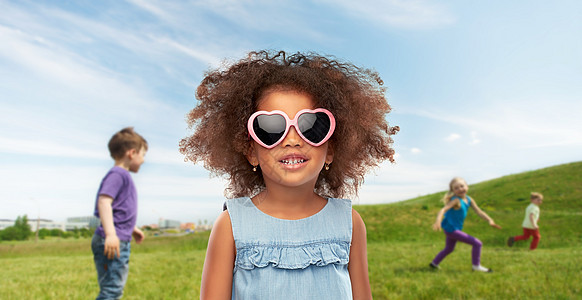 童年夏天的快乐的小非裔美国女孩心形太阳镜超过儿童草地背景下玩夏天戴太阳镜的非洲小女孩图片