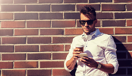 技术人的年轻人戴太阳镜,智能手机咖啡杯城市街道城市街道上有智能手机咖啡杯的男人图片