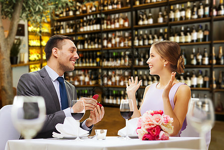 求婚,情侣情人节兴奋的年轻女人看着男人与订婚戒指餐厅或酒吧背景餐馆向快乐的女人求婚的男人图片