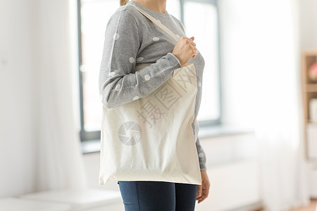 消费主义生态友好的女与白色可重复用的帆布袋,用于灰色背景下的食品购物妇女与可重复用的帆布袋食品购物图片