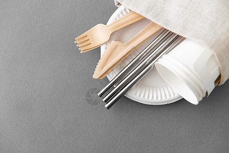 循环利用环保套木制叉子刀具纸杯金属吸管,盘子上有灰色背景的餐巾盘子上的木制叉子刀子纸杯图片