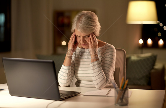 技术,老年压力疲惫或压力大的老年妇女,有笔记本电脑,晚上家头痛疲惫的高级女人晚上家带笔记本电脑图片