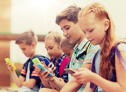 小学教育,友谊,童年,技术人的群快乐的小学生,智能手机背包坐户外长凳上有智能手机的小学生图片