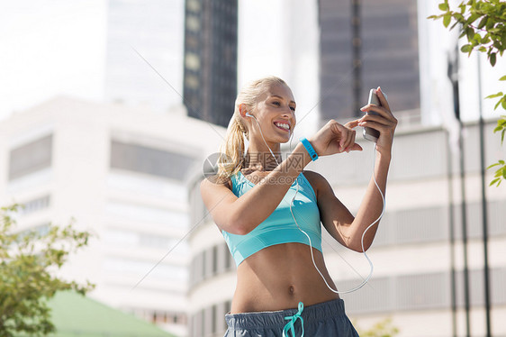 健身,运动人的微笑的年轻妇女与智能手机耳机,听音乐锻炼城市街道的背景城市里有智能手机耳机的快乐女人图片