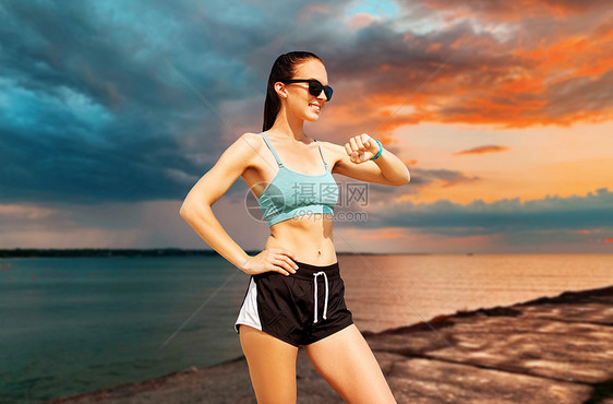 运动,技术健康的生活方式微笑的年轻妇女与健身跟踪器海上日落天空背景快乐的女人夏天的海滩上有健身追踪器图片