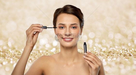 美丽,化妆化妆品的美丽的年轻女人涂睫毛膏闪闪发光的金色闪光的背景美丽的女人涂睫毛膏图片