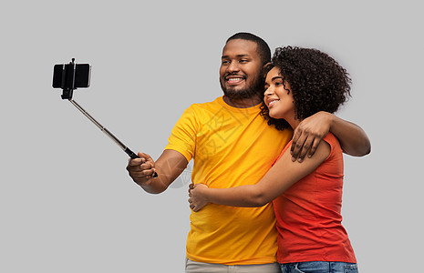 关系人的快乐的非裔美国人夫妇用智能手机灰色背景的自拍杆上拍照非裔美国夫妇用手机自拍图片