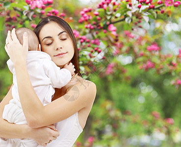 家庭母亲的快乐的微笑年轻母亲与小婴儿自然春天樱花背景母亲带着孩子春天的花园背景下图片