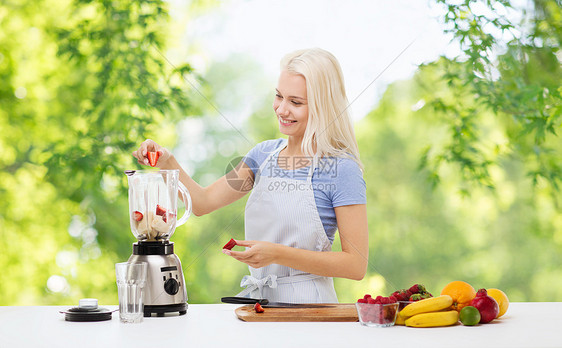 健康的饮食,烹饪,食物人的快乐的微笑年轻妇女,把水果浆果水果冰沙搅拌机绿色的自然背景微笑的女人用搅拌机做水果奶昔图片