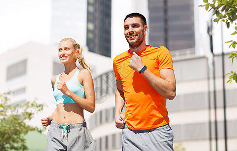 运动,健康的生活方式人们的微笑的夫妇健身跟踪者夏季城市街道的背景上跑步快乐的夫妇与健身跟踪者城市跑步图片