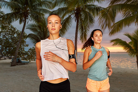 健身,运动健康的生活方式年轻的妇女或女朋友戴着带智能手机的,热带海滩上奔跑棕榈树上带着耳机智能手机的年轻图片