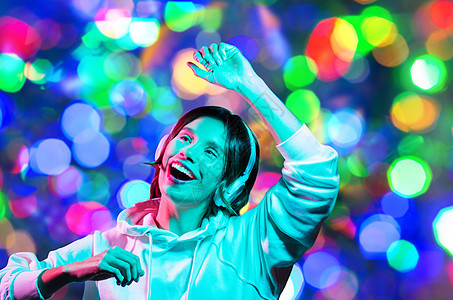 夜生活,技术人的快乐的年轻女人戴着帽衫听音乐跳舞夜间灯光背景戴耳机的女人夜灯上跳舞图片
