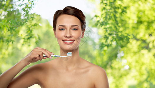 口腔卫生,牙科护理健康理念微笑的女人用牙刷清洁牙齿绿色自然背景微笑的女人用牙刷清洁牙齿图片