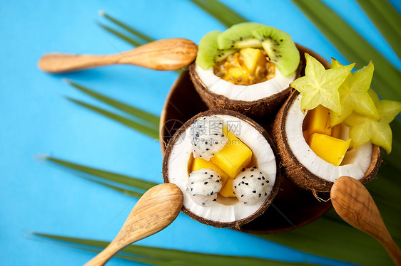 食物,夏天健康的饮食混合同的异国水果椰子壳的盘子与木制勺子绿色风扇棕榈叶蓝色背景用勺子混合椰子壳里的异国水果图片