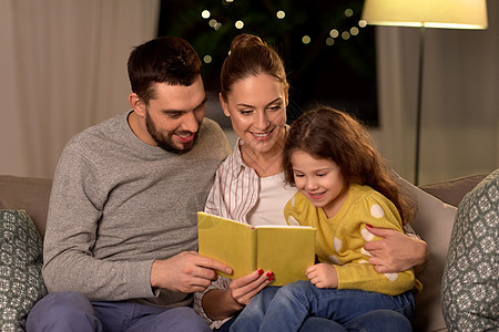 家庭休闲人的快乐的父亲母亲小女儿晚上家看书晚上家快乐的家庭读物图片