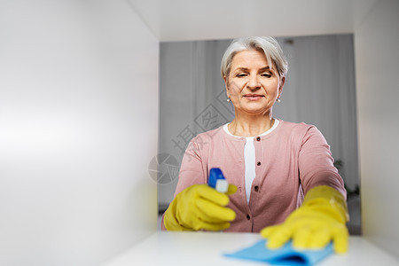 人,家务家务快乐的高级妇女与灰尘布洗涤剂清洁架家里快乐的高级女人,家里有布尘架图片