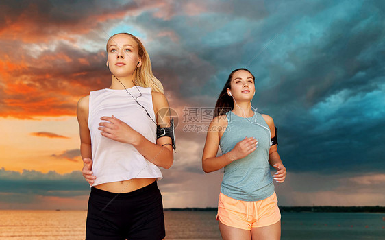 健身,运动健康的生活方式年轻的妇女或女朋友戴着带智能手机的,背景上跑过大海日落的天空带着耳机智能手机的年图片