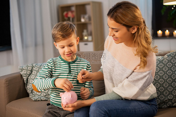 金钱家庭人的快乐的微笑母亲节俭的小儿子把欧元硬币放家里的储蓄罐里妈妈小儿子家带着储蓄罐图片