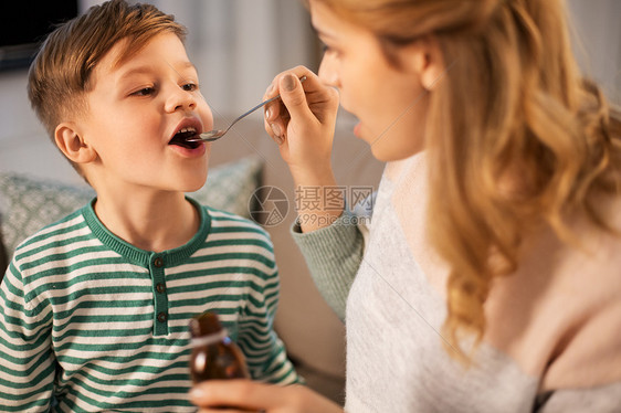 家庭健康人的悲伤的母亲家里给生病的小儿子服用解热药或止咳糖浆母亲给生病的儿子吃药或止咳糖浆图片