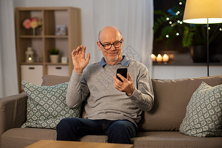 技术,老年人人的快乐的微笑秃顶老人与智能手机有视频电话挥手家里晚上有智能手机的老人家有视频通话图片