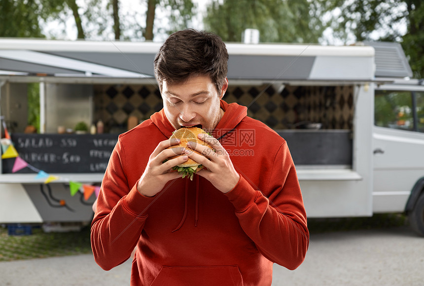 快餐,外卖人们的饥饿的年轻人穿着红色帽衫,街头背景的食品卡车上吃外卖汉堡包饥饿的年轻人食品卡车上吃汉堡包图片