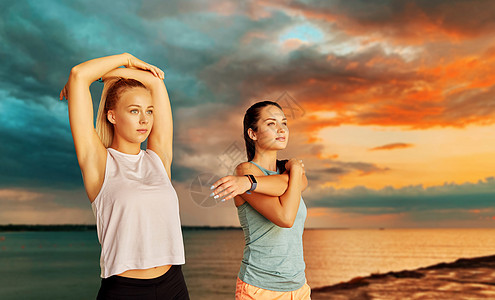 健身,运动健康的生活方式微笑的年轻妇女或女朋友与活动跟踪者伸展海上日落天空的背景有健身追踪器的女人海上伸展图片