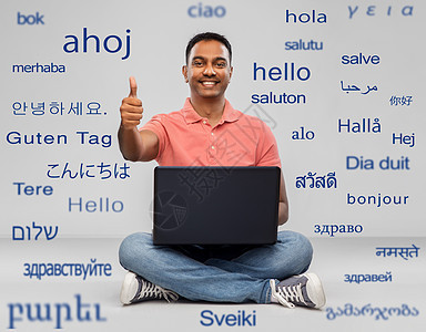 技术,沟通人的快乐的印度男人,笔记本电脑坐地板上,灰色背景下用同的外语问候语快乐的印度男人,带着笔记本电脑,竖图片