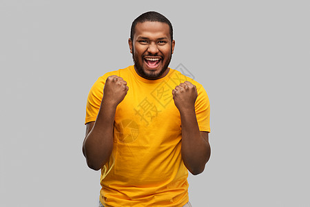 人们的微笑的年轻非裔美国人穿黄色T恤庆祝成功的灰色背景微笑的非裔美国人庆祝成功图片