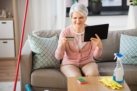 家庭技术快乐的高级妇女与平板电脑信用卡后,清洁家庭家里有平板电脑信用卡的老妇人图片