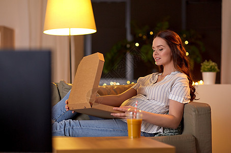 怀孕,休闲人们的快乐的微笑孕妇沙发上看电视家吃外卖比萨饼孕妇带着披萨盒家看电视背景图片