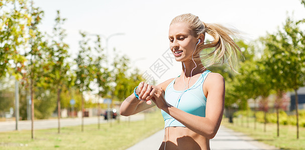 体育,技术人的微笑的年轻妇女与健身跟踪耳机城市街道上锻炼的背景快乐的女人有健身追踪器耳机图片