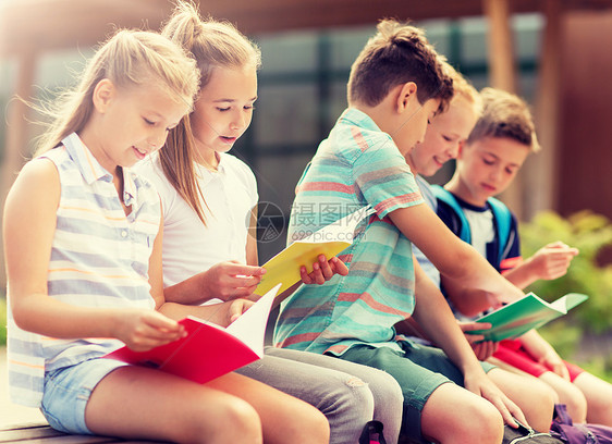 一群快乐的小学生坐户外长凳上看书图片