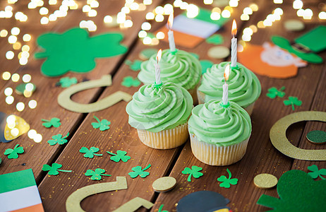 圣帕特里克日,假日庆祝绿色纸杯蛋糕与蜡烛,马蹄三叶草木制桌子上的节日灯绿色纸杯蛋糕圣帕特里克日装饰品图片