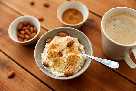 食物早餐燕麦粥碗与切片香蕉,杏仁坚果肉桂杯咖啡木桌上木制桌子上有香蕉杏仁的燕麦片背景图片