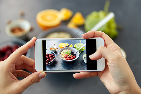 食物,饮食早餐的妇女的手碗中拍摄谷物与水果,浆果果汁与智能手机用智能手机拍照早餐图片