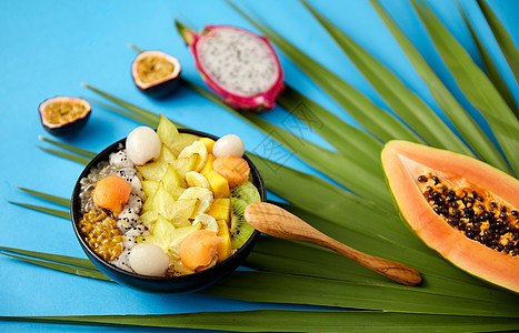 食物,夏天健康的饮食混合同的异国水果碗与木勺绿色风扇棕榈叶蓝色背景用木勺把异国水果混合碗里图片