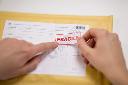送货邮件服务人员装运妇女的手邮局的信封上贴着易碎的标记把易碎的痕迹粘信封里的包裹上图片
