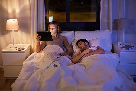 使用平板电脑工作看文件的妇女与男人在卧室床上图片