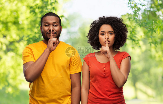 沉默,秘密保密的快乐的非裔美国人夫妇绿色的自然背景下做着嘘声的手势快乐的非裔美国夫妇做着嘘声的手势图片