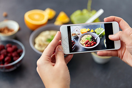 食物,饮食早餐的妇女的手碗中拍摄谷物与水果,浆果果汁与智能手机用智能手机拍照早餐图片