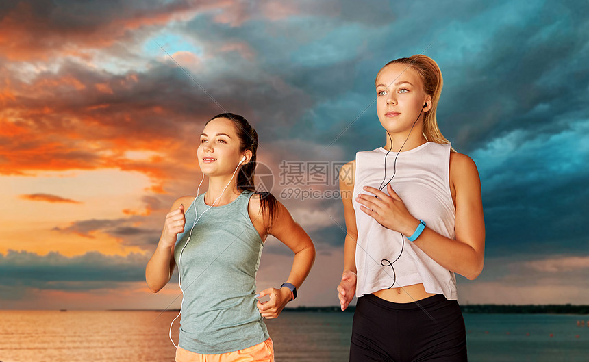 健身,运动健康的生活方式年轻的妇女或女朋友,耳机海上日落日落天空的背景有耳机运行的女或女朋友图片